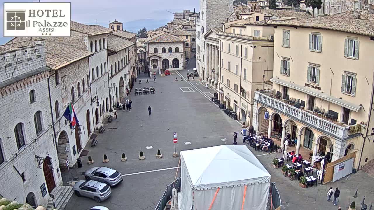 A large, mostly empty town square is surrounded by several multi-story buildings, under an overcast sky.