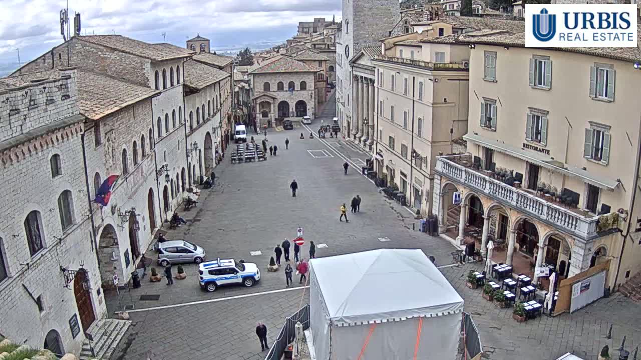 A large, mostly empty town square is surrounded by old stone buildings under an overcast sky.