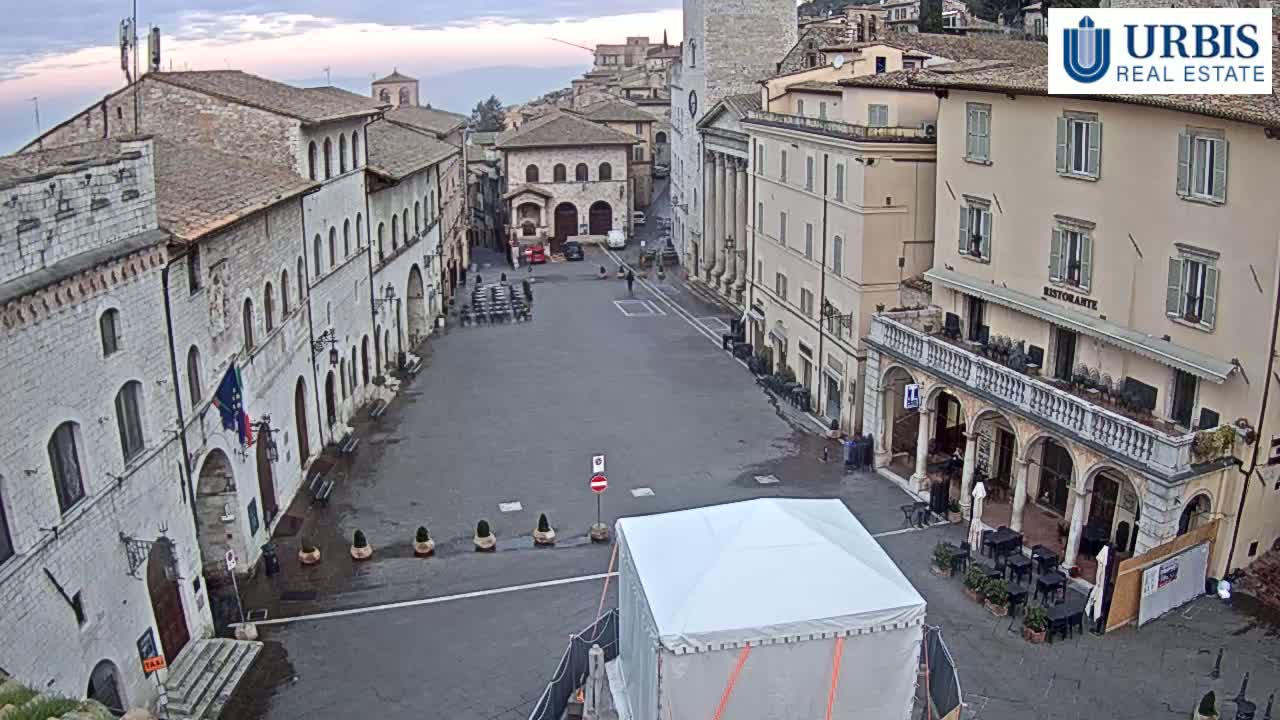 A large, empty town square is surrounded by historic stone buildings under an overcast sky.