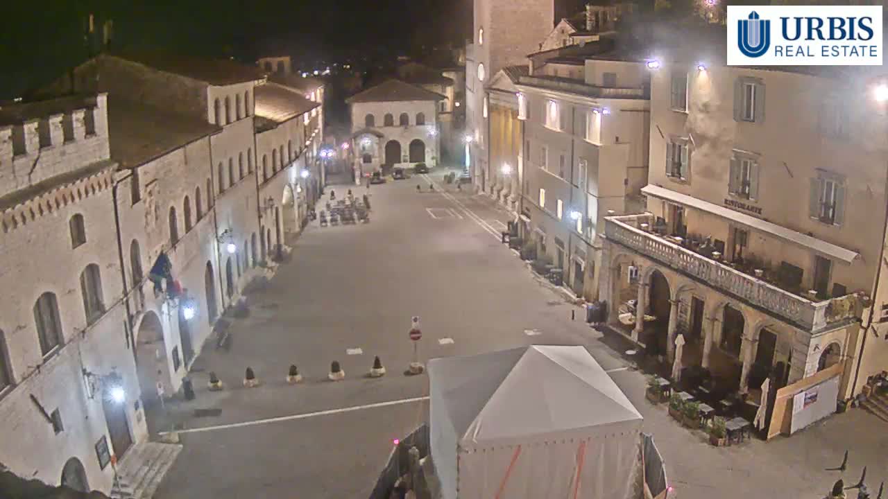 A mostly empty town square at night, surrounded by illuminated stone buildings.