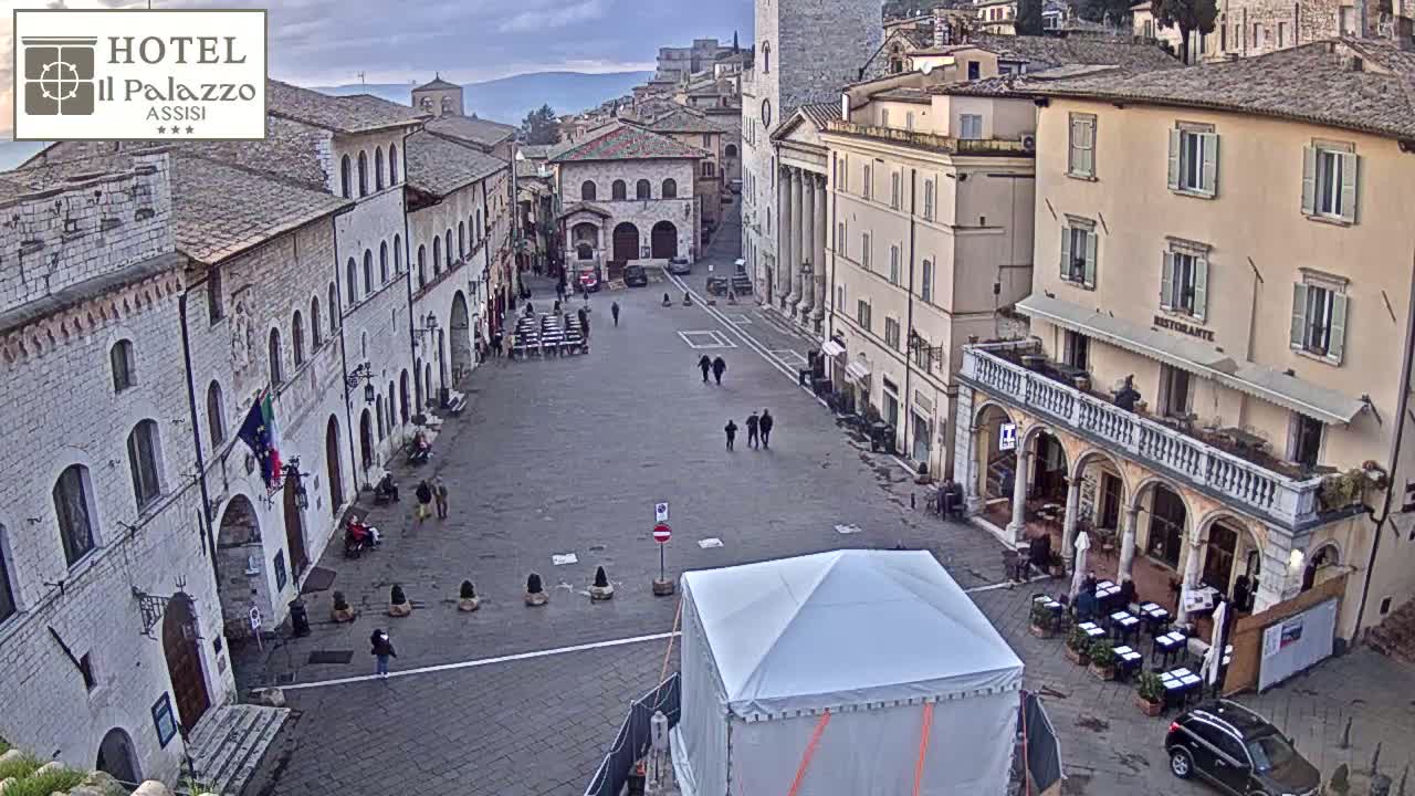 A large, mostly empty town square with several stone buildings and a white tent in the center, under a cloudy sky.