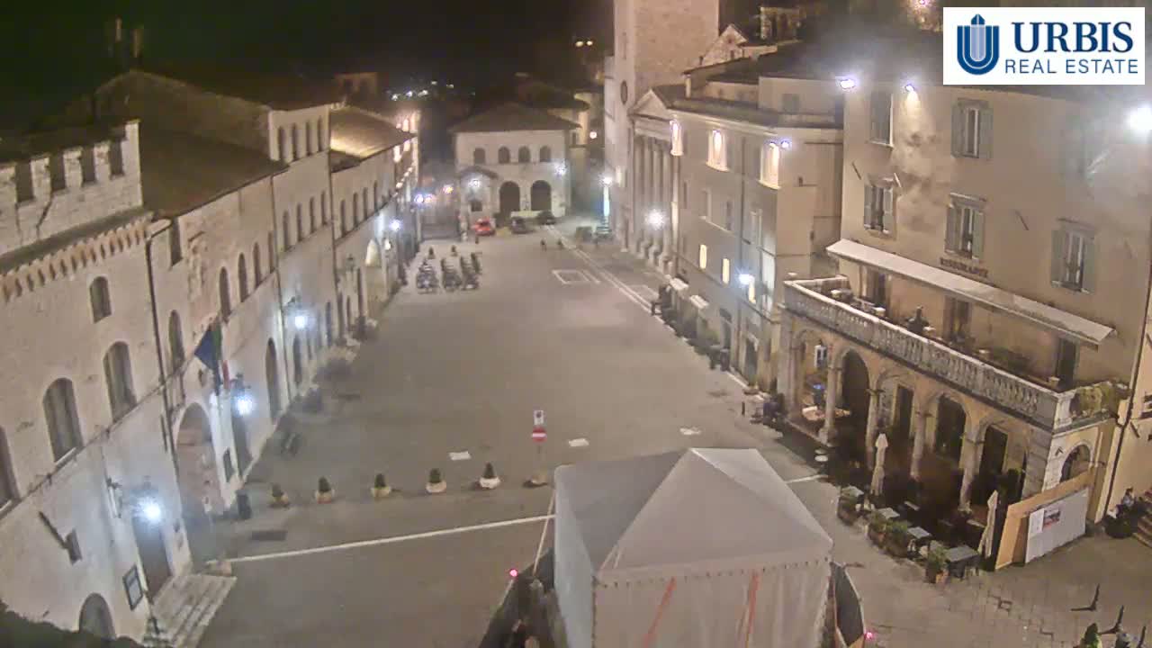 A nighttime, high-angle view of a mostly empty town square surrounded by historic-looking buildings.