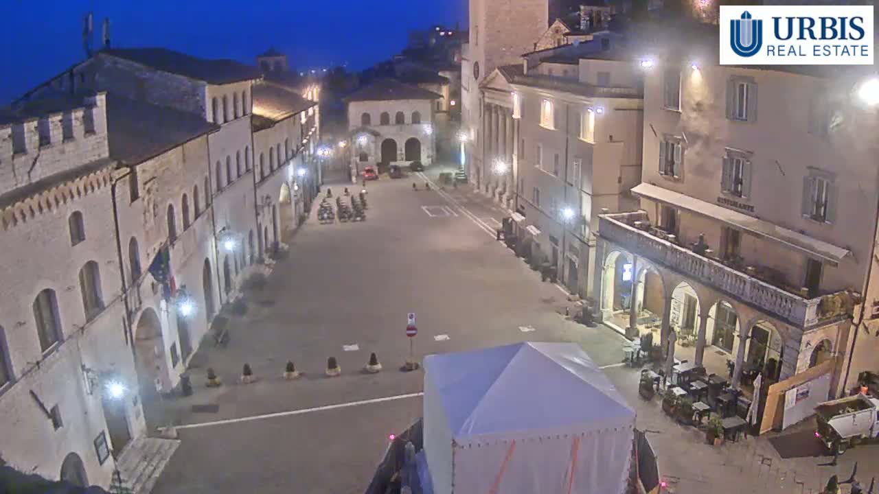 A mostly empty town square at night, surrounded by old stone buildings under a dark blue sky.