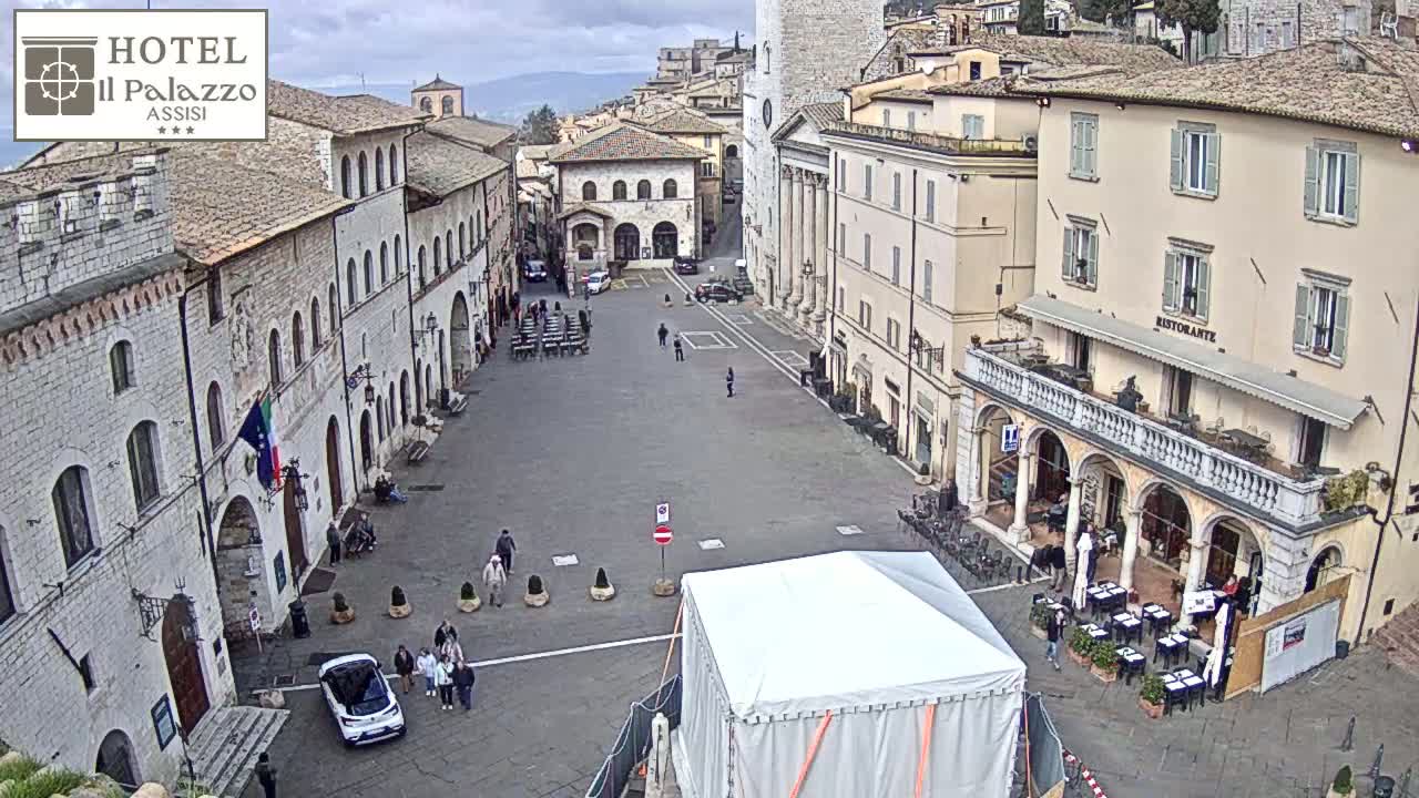 A large, mostly empty town square is surrounded by stone buildings under an overcast sky.