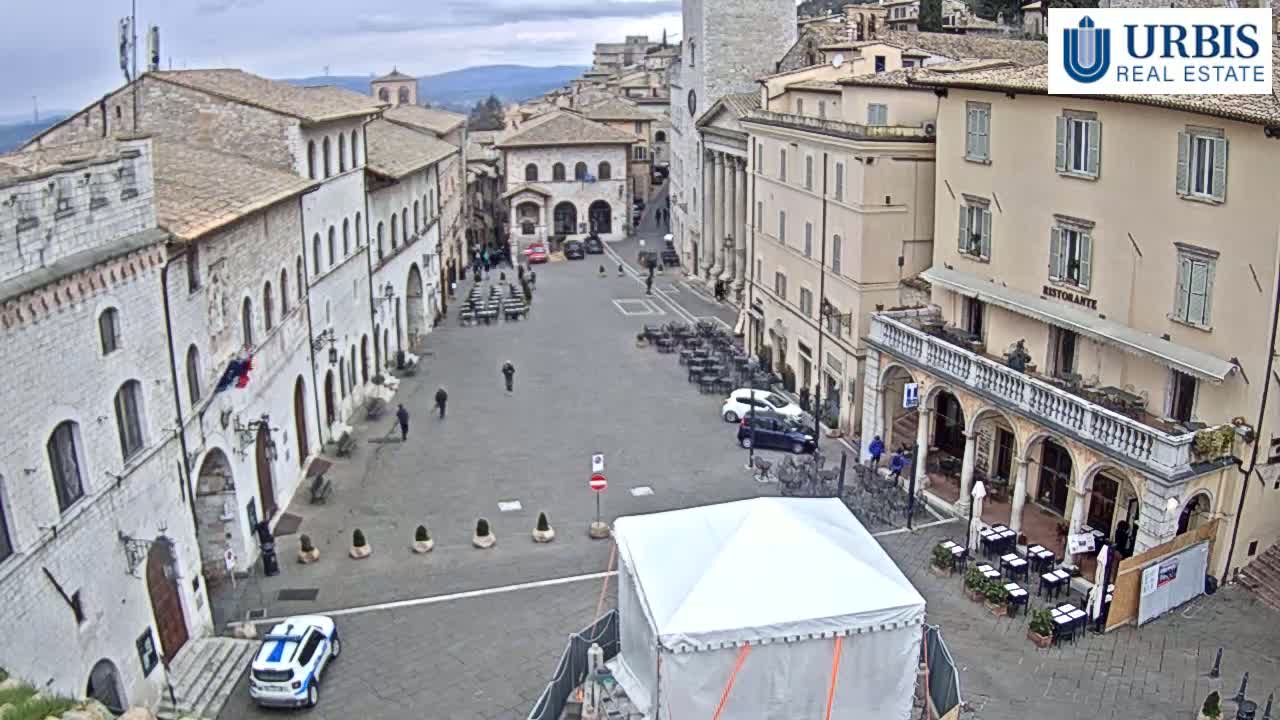 A mostly empty town square, surrounded by historic stone buildings, under an overcast sky.
