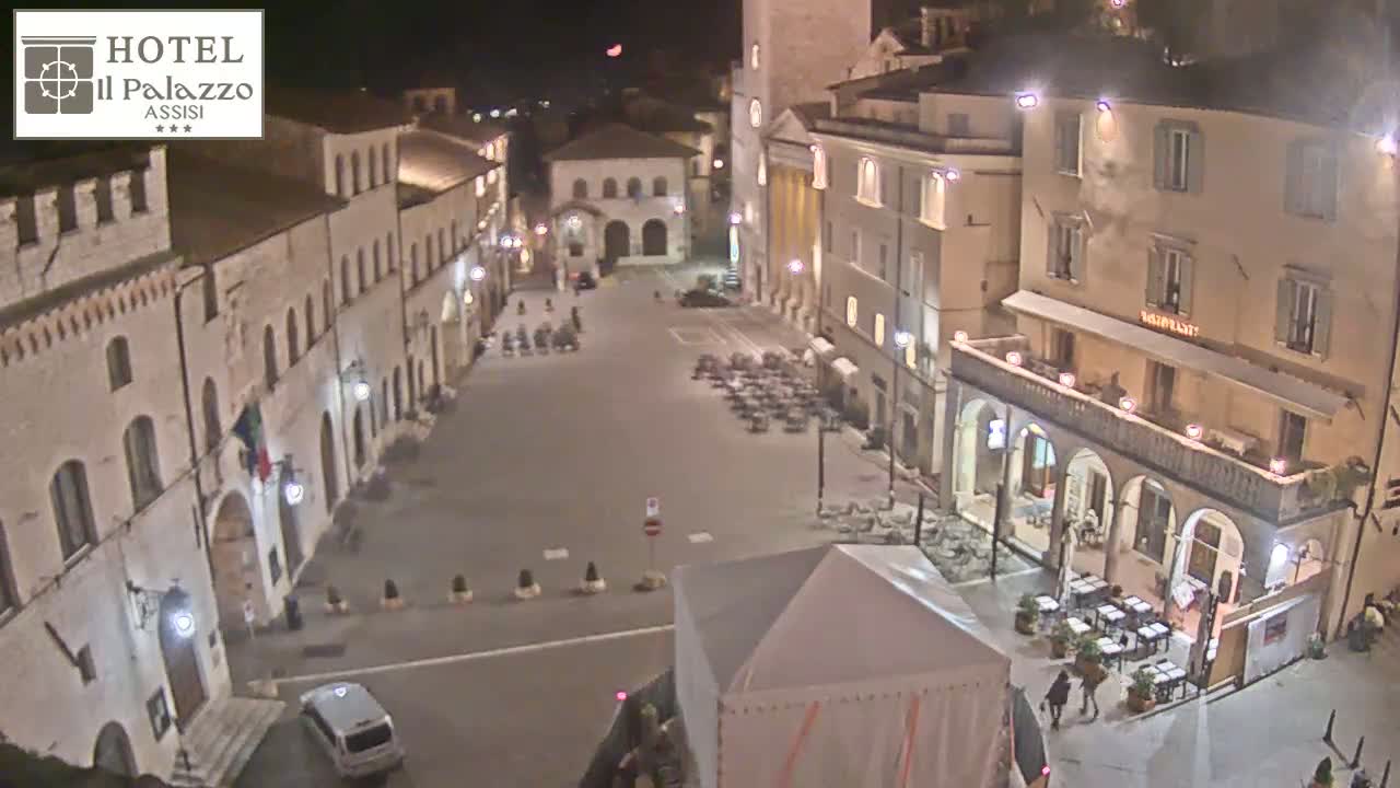 A nighttime view of a mostly empty town square surrounded by historical buildings, under a clear sky.