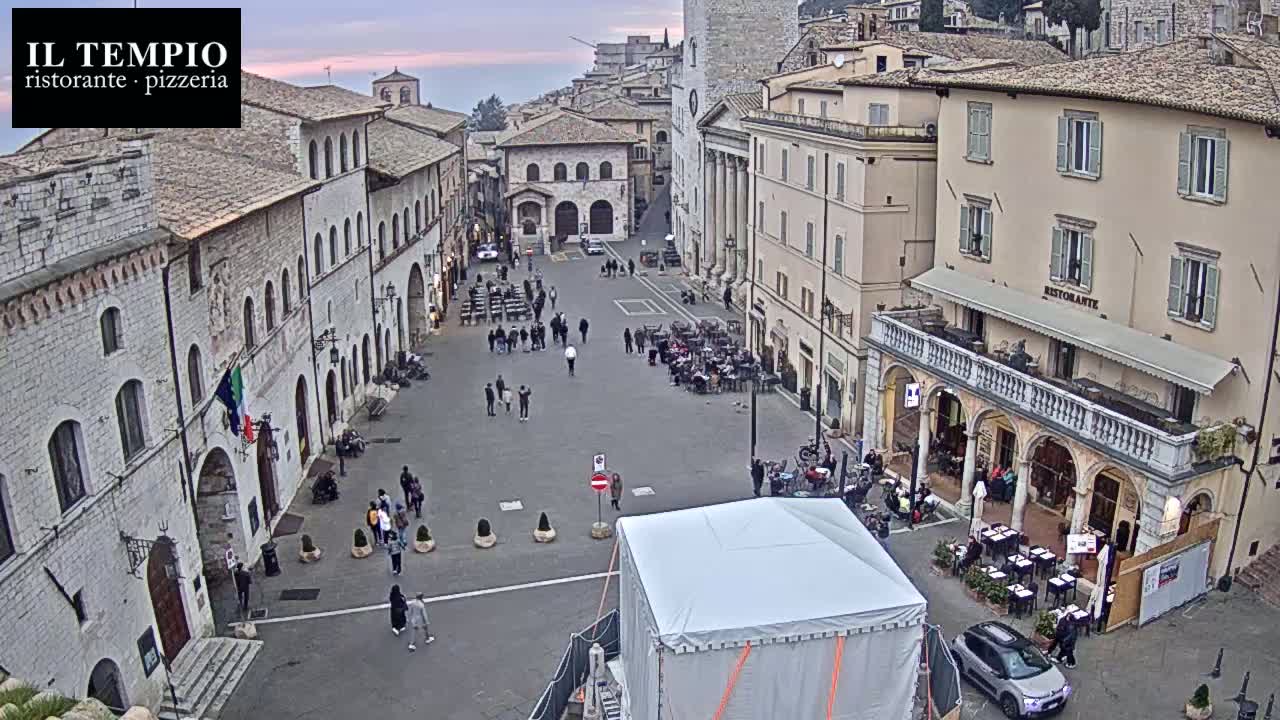 A large, mostly empty town square with stone buildings on all sides, under a twilight sky.