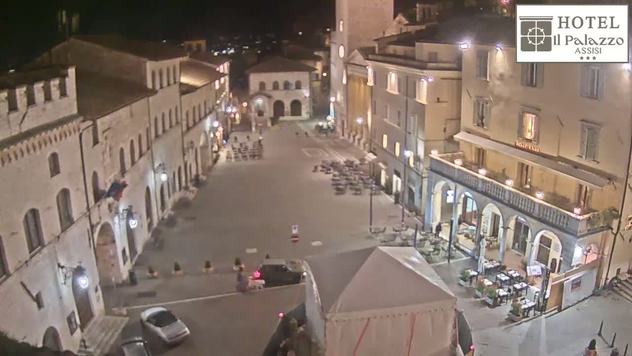 A nighttime, high-angle view of a town square with several buildings surrounding it, some with outdoor seating areas.