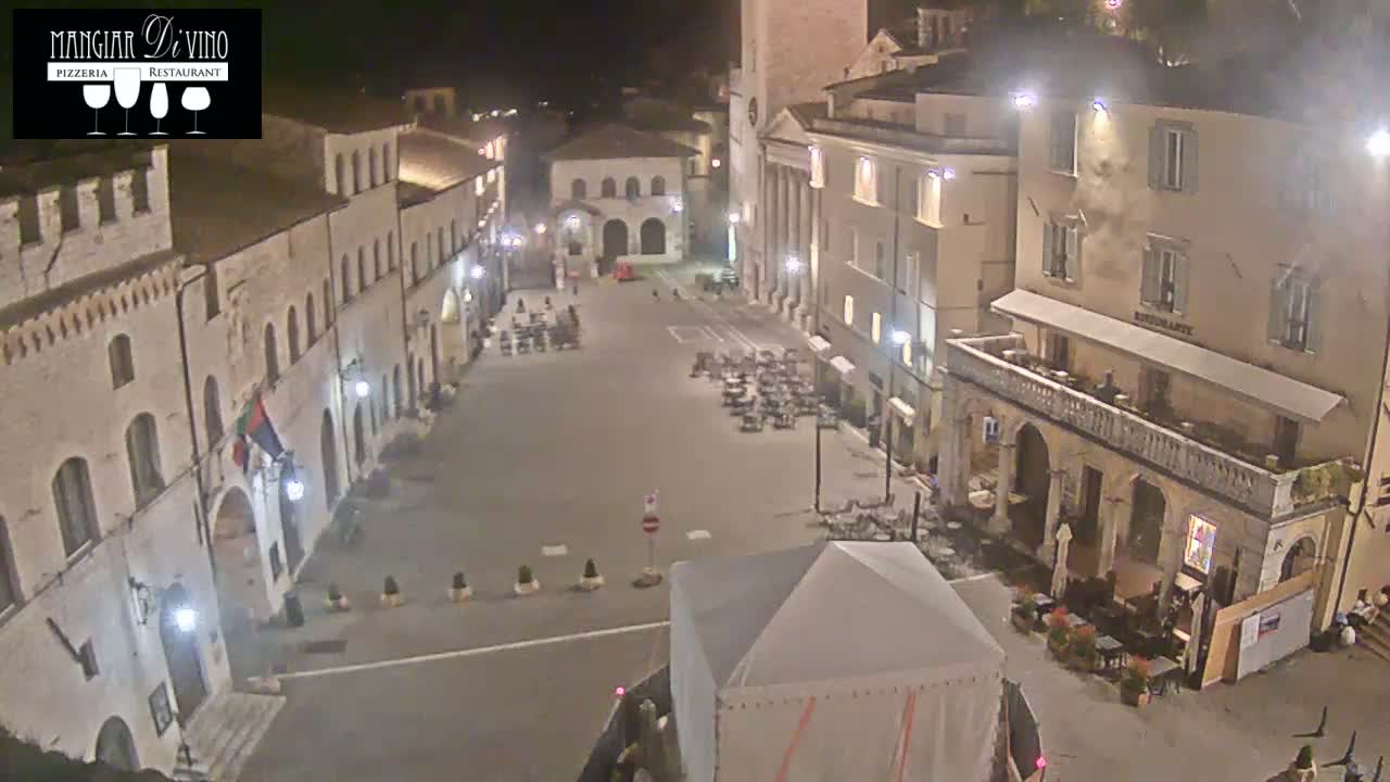 A mostly empty town square at night, illuminated by streetlights, is surrounded by old stone buildings.