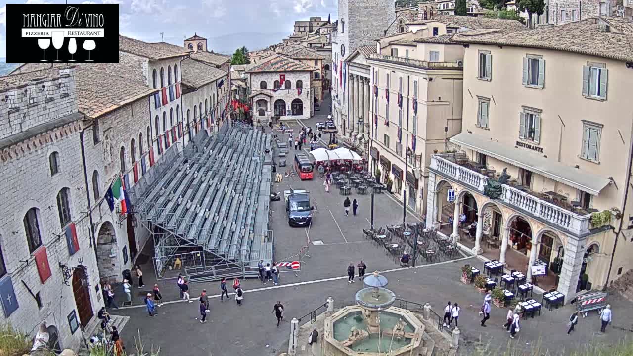 A town square with temporary bleachers, a fountain, and several people milling about under an overcast sky.