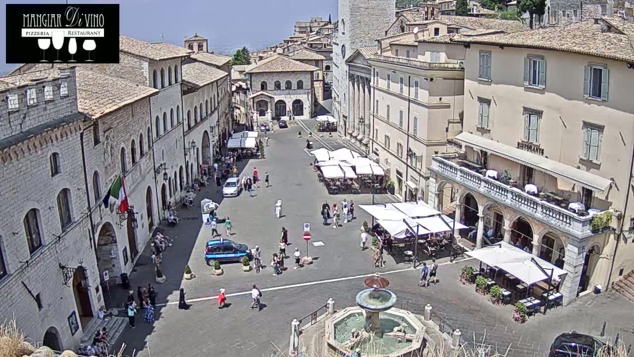 A sunny town square in Italy is filled with people, outdoor seating, and a central fountain.