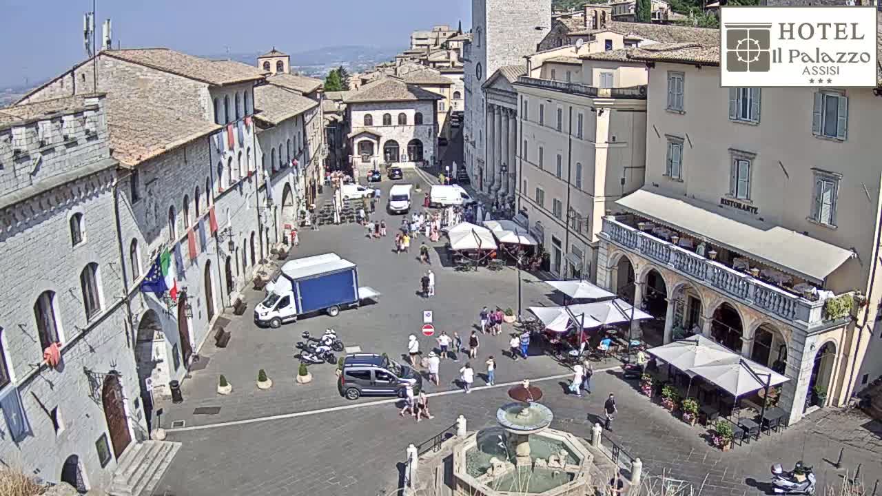 A sunny town square in Italy, filled with people, vehicles, and outdoor seating areas surrounding a central fountain.