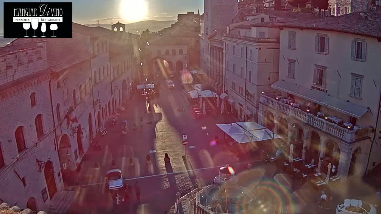 A sun-drenched town square, filled with people and outdoor seating at restaurants, is viewed from above at sunset.