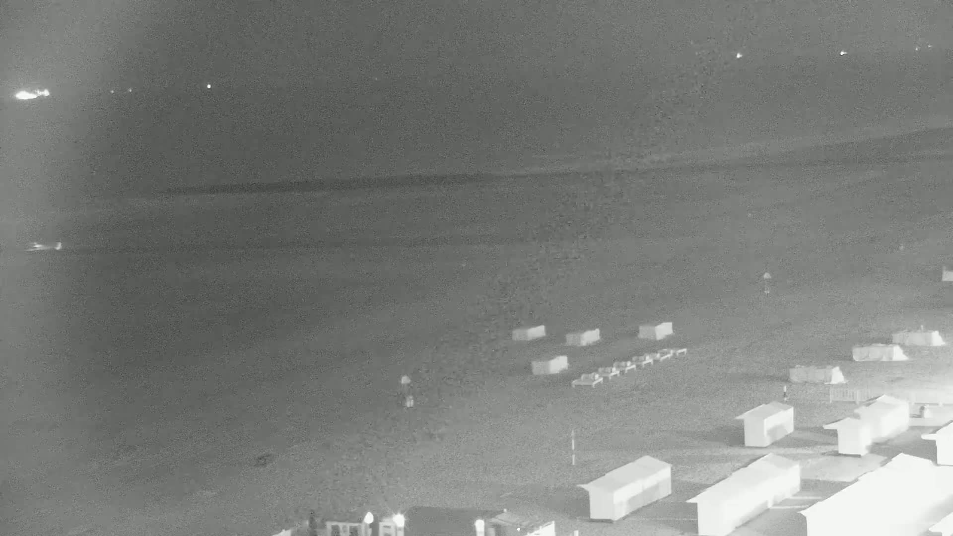 A dark beach at night with several small structures and a few people visible under a clear sky.