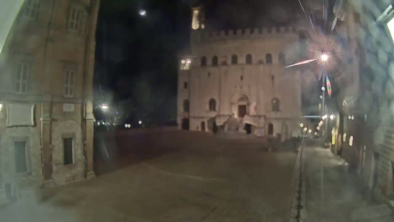 A nighttime view of a town square with a large stone building and adjacent buildings, illuminated by streetlights.