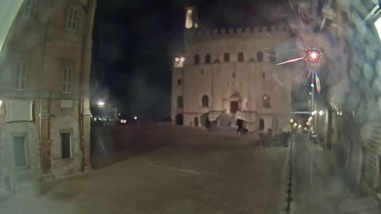A nighttime view of a town square with old buildings, seen through a cracked windshield.