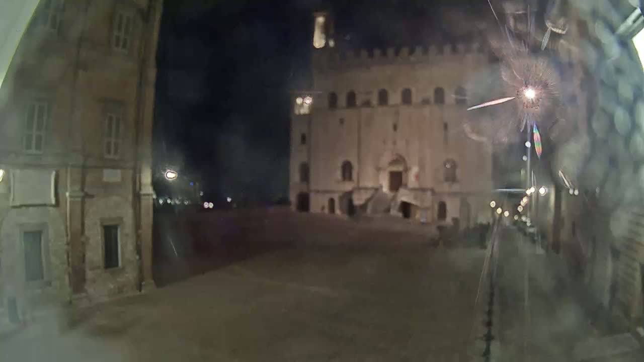 A nighttime view of a town square with a large stone building and flanking structures.