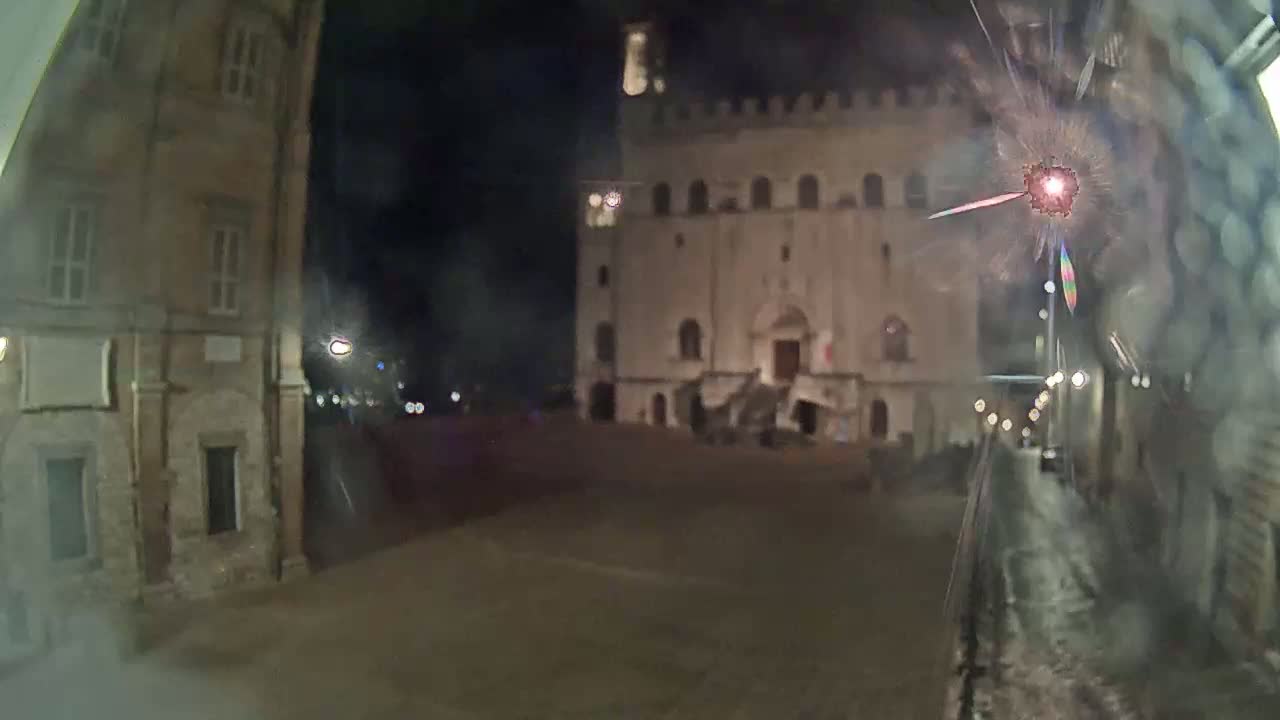 A nighttime view of a large stone building in a town square, with fireworks visible in the foreground.