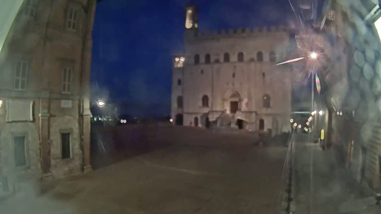 A large, light-colored stone building with a staircase stands in a dimly lit town square at night.