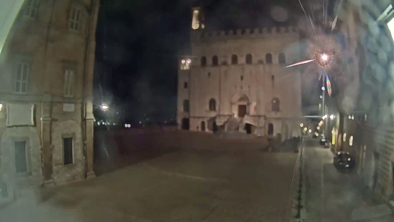A nighttime view of a town square, showing a large stone building at the end of a street, with a cracked window in the foreground.