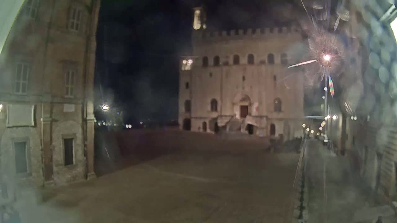A nighttime view of a large stone building, possibly a palace or civic building, in a town square, with a few lights visible and a blurry effect from what might be rain or condensation on the lens.