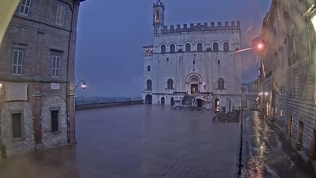 A large stone building stands in a town square, which is flooded by heavy rain under a dark, overcast sky.
