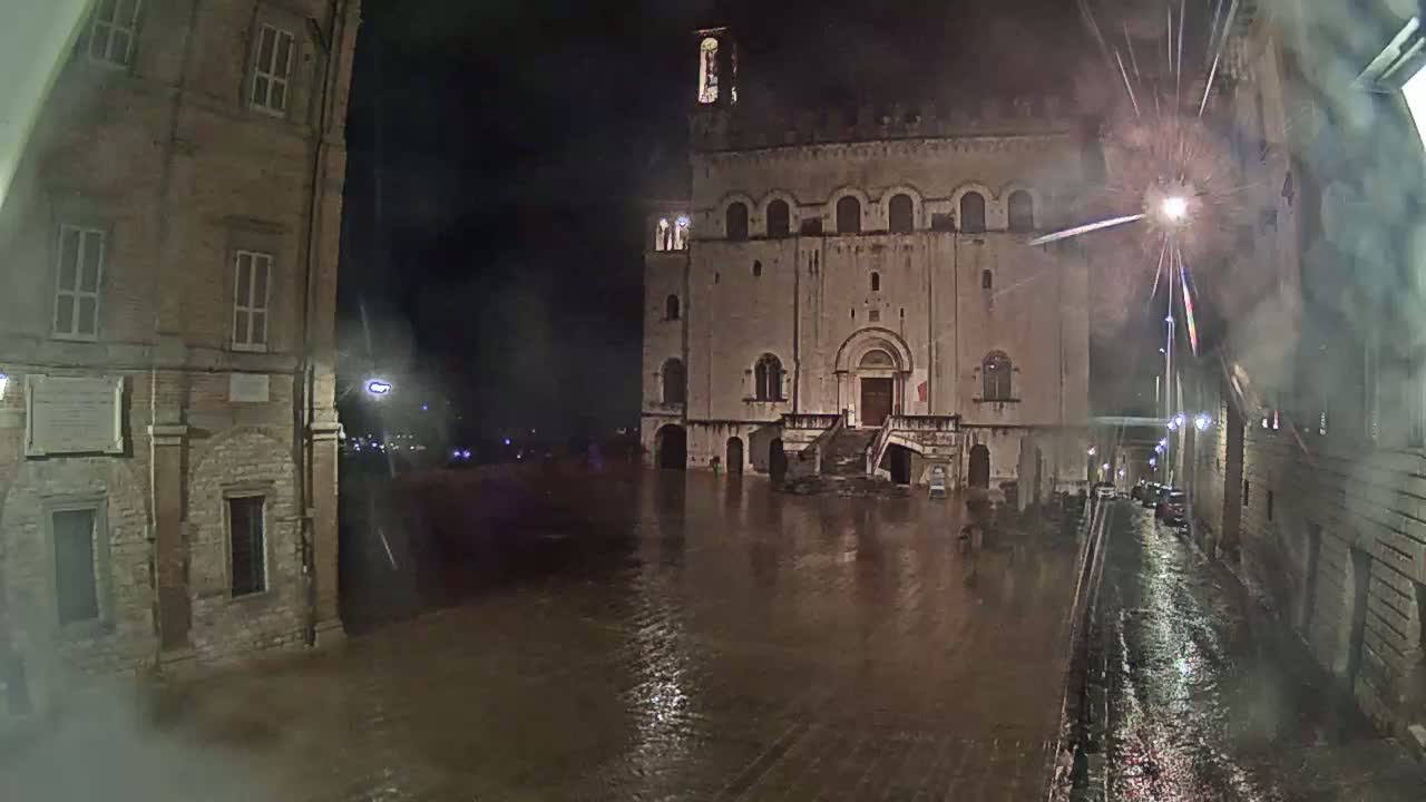 A large, stone building stands in a flood-covered square at night during a heavy rainstorm.