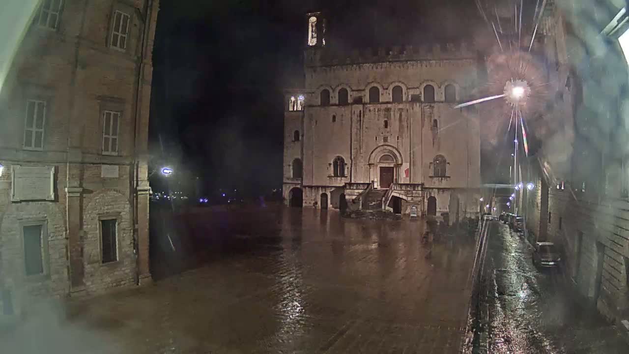 A large stone building is partially submerged in floodwaters at night, with rain falling and streetlights illuminating the scene.