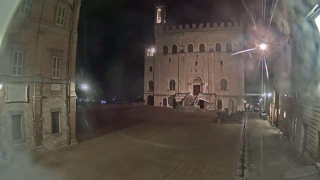 A large, stone building with a staircase stands in a square at night, illuminated by streetlights.