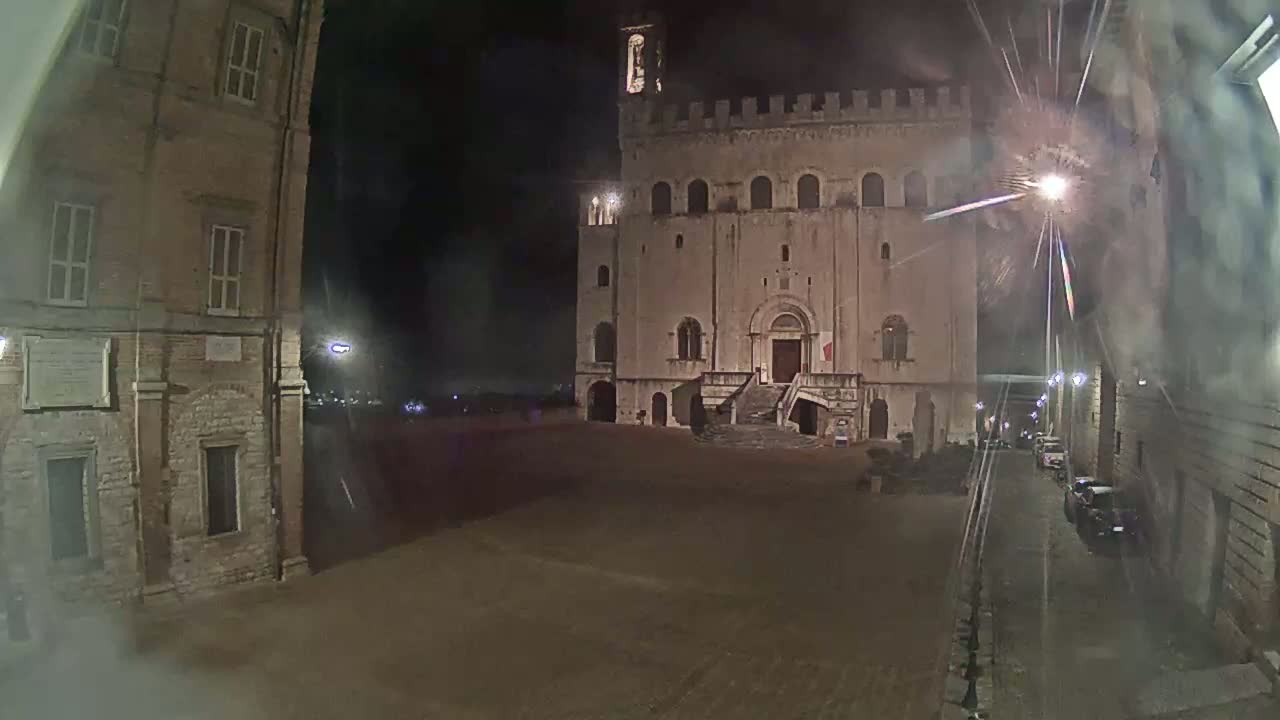 A large, stone building with a staircase stands in a dimly lit, empty square at night.