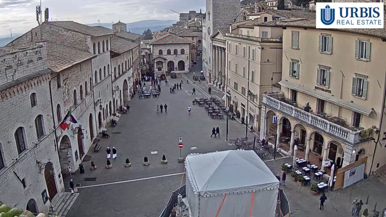A large, mostly empty town square is surrounded by stone buildings under an overcast sky.