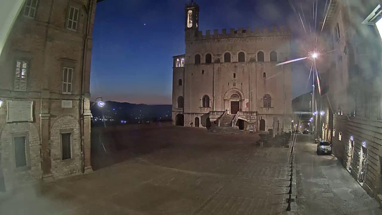 A large, stone building with a clock tower stands in a dimly lit, empty square at twilight.