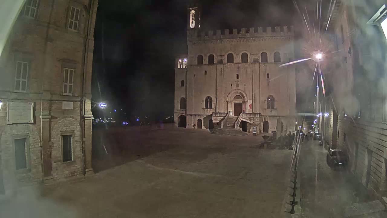 A large, stone building with a staircase stands in a dimly lit square at night, under a hazy sky.