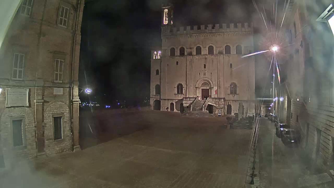 A large, stone building with a staircase stands in a plaza at night, under a hazy sky.