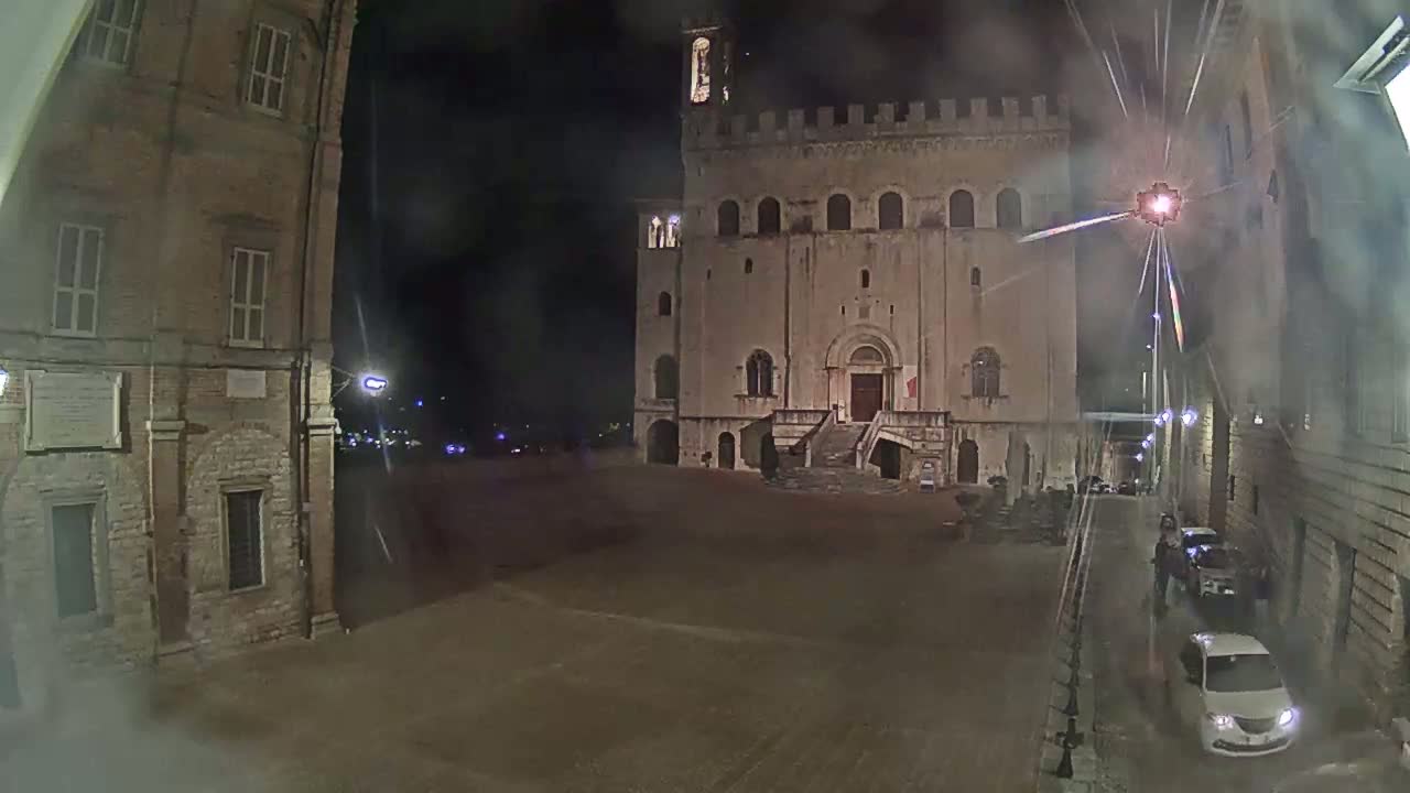 A large, stone building stands in a sparsely populated square at night, under hazy conditions.