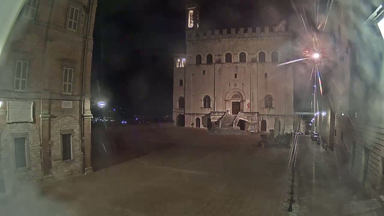 A large, stone building with a staircase stands in a dimly lit, empty square at night.