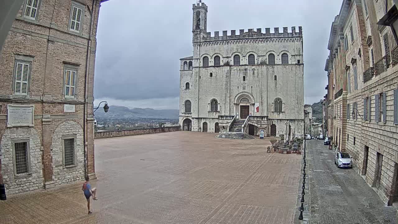 A person jogs across a large, empty plaza in front of a medieval-style building on an overcast day.