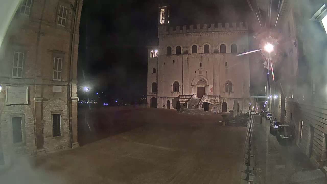 A large, stone building with a staircase stands in a mostly empty square at night, illuminated by streetlights.