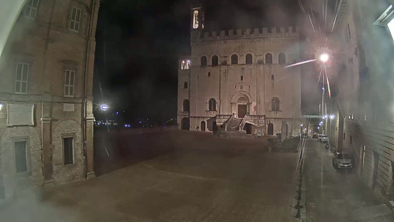 A large, stone building with a staircase stands in a dimly lit, empty square at night.