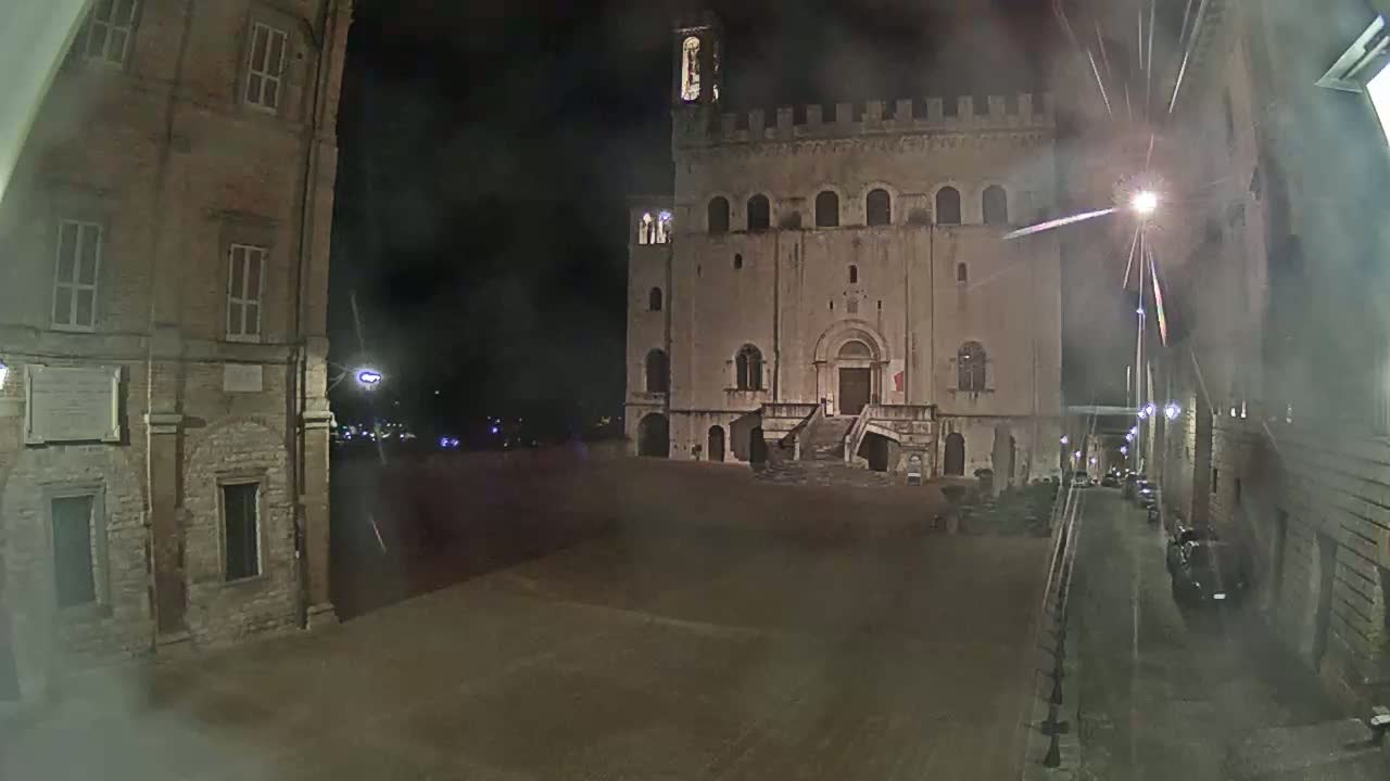 A large, stone building with a staircase stands in a dimly lit square at night, under hazy or foggy conditions.