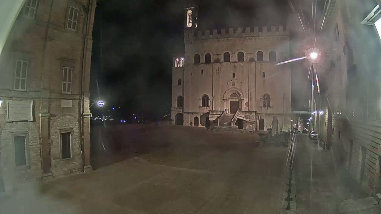A large, stone building with a staircase stands in a dimly lit, empty square at night, under hazy conditions.