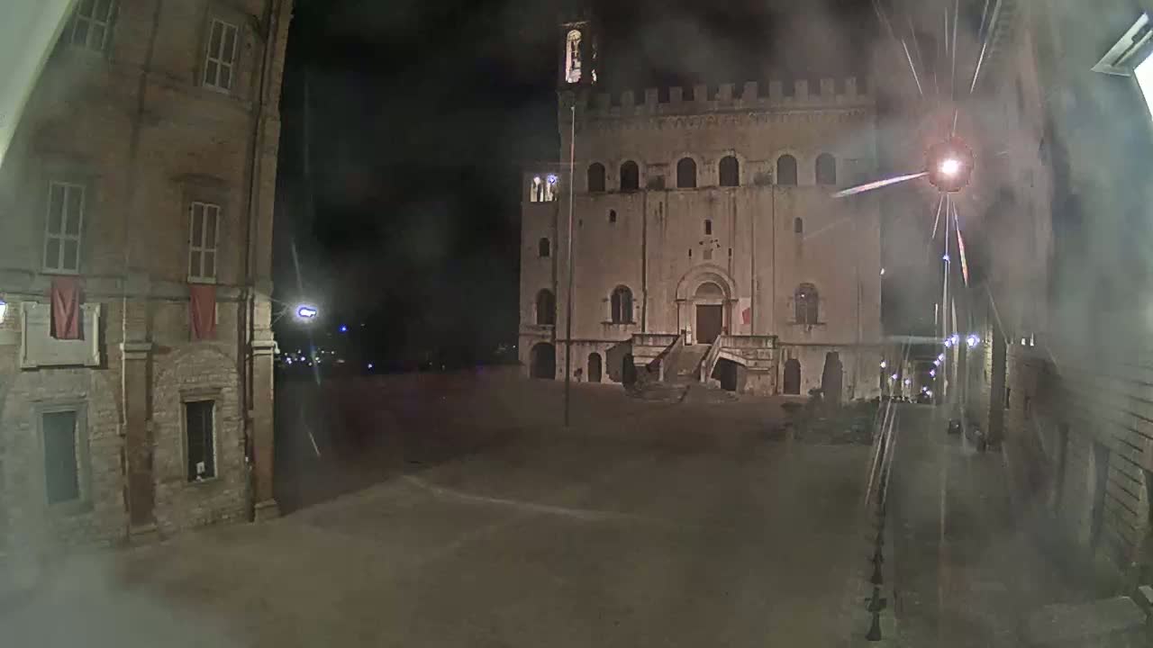A large stone building with a staircase stands in a dimly lit square at night, under hazy conditions.