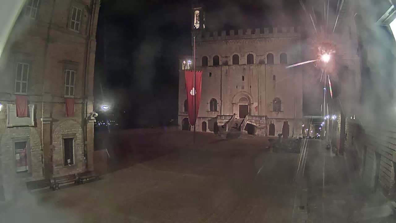 A nighttime view of a town square with a large stone building, flanked by smaller buildings, and a red banner in the center.