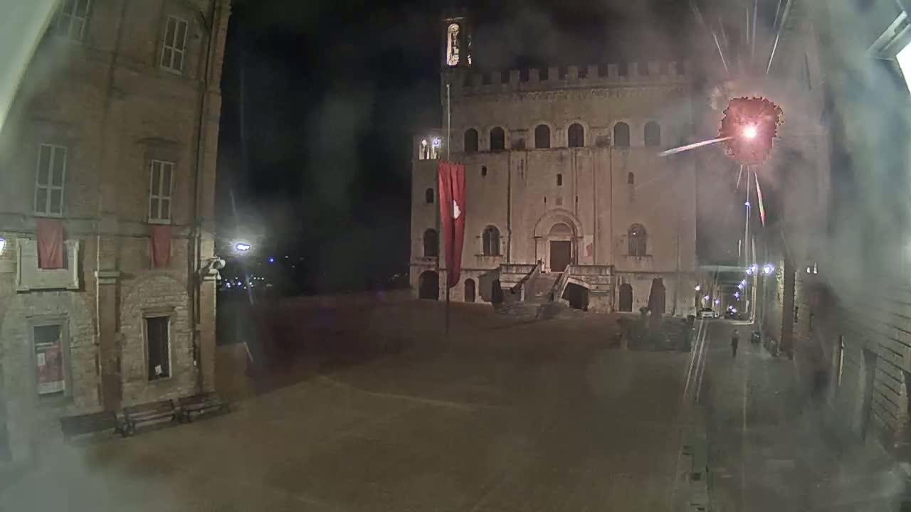 A nighttime view of a town square with an old stone building and a fireworks display.