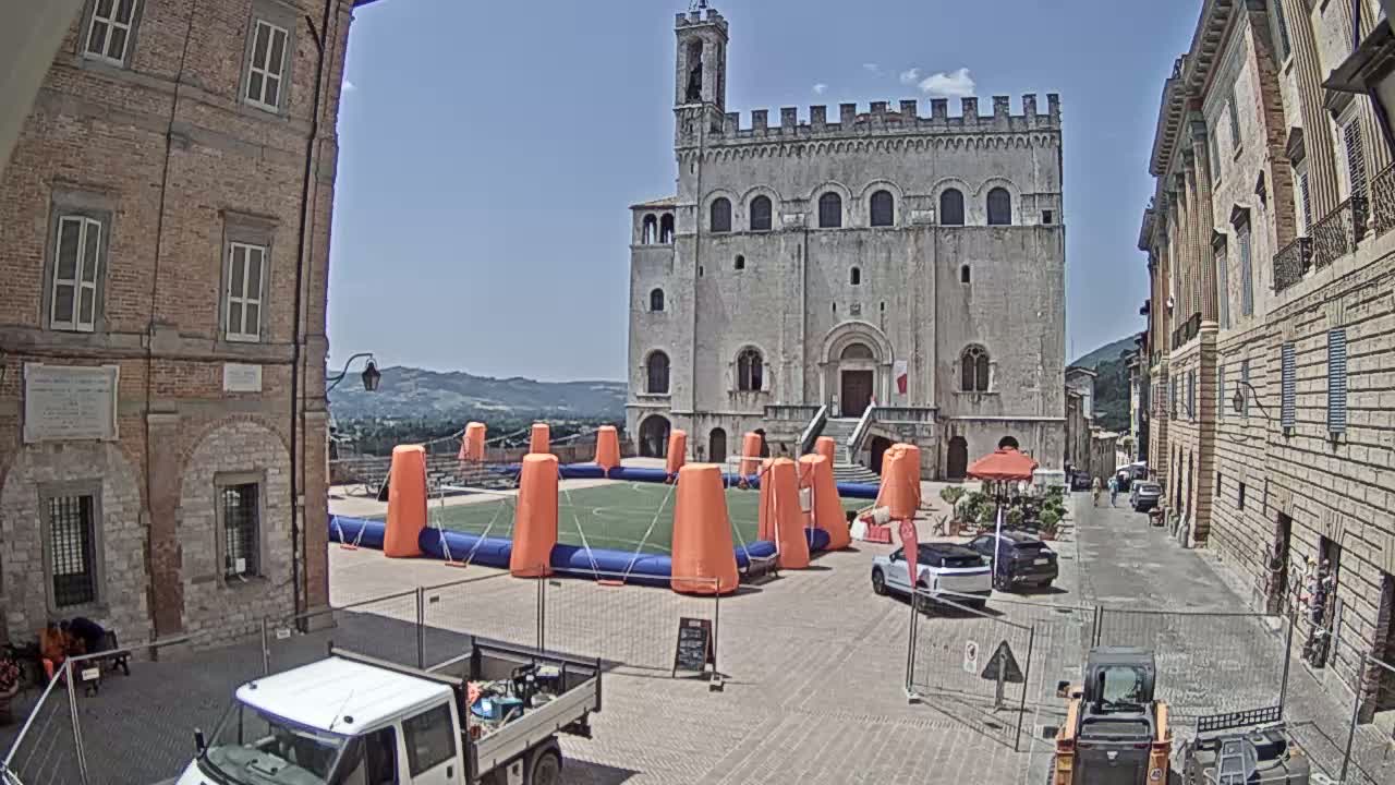 A temporary inflatable soccer field is set up in a town square on a sunny day, between two historic brick buildings and under a mostly clear sky.