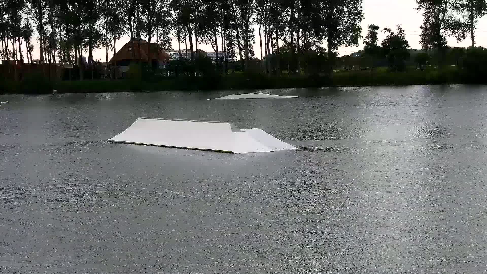 A calm body of water reflects the surrounding vegetation and a small, floating dock with numerous yellow cables extending from behind it.