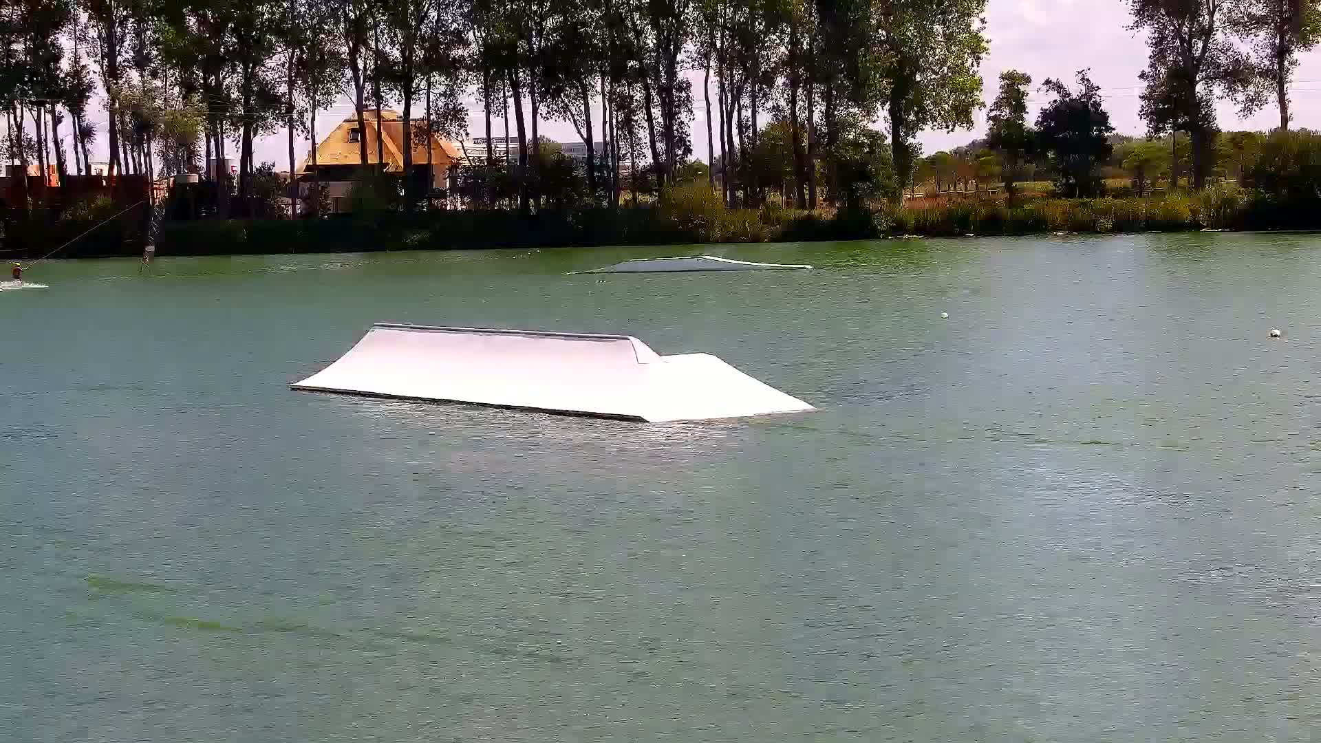 A calm body of water reflects the surrounding vegetation and a small, floating dock with numerous yellow cables extending from behind it.