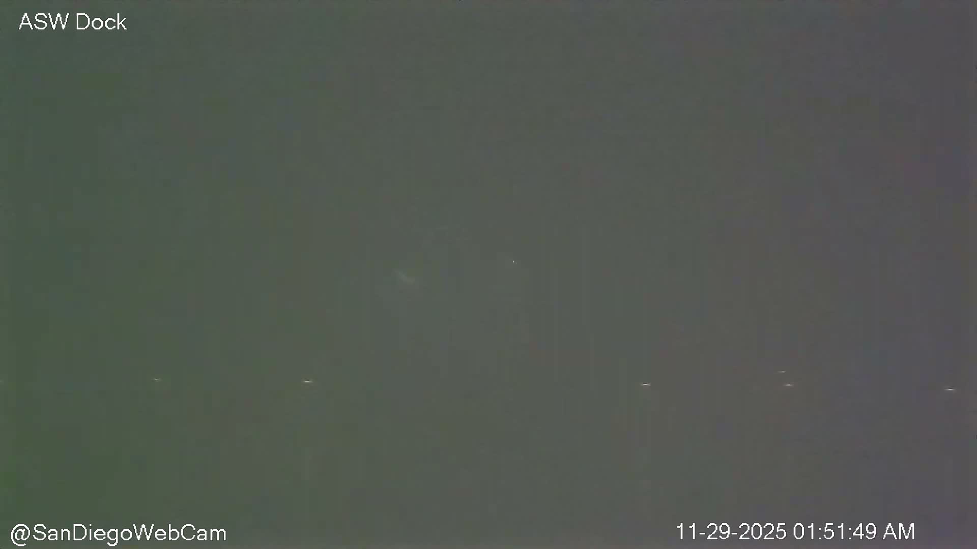 A very dark and foggy outdoor scene at night shows only a few faint, distant lights through the heavy atmospheric obscurity.