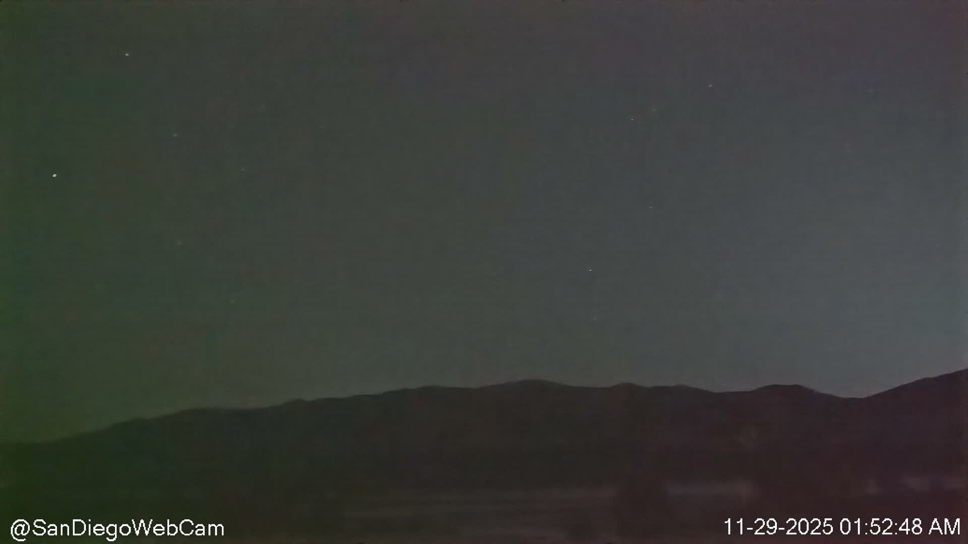 A clear night sky, sparsely dotted with faint stars, stretches above a dark, silhouetted mountain range.
