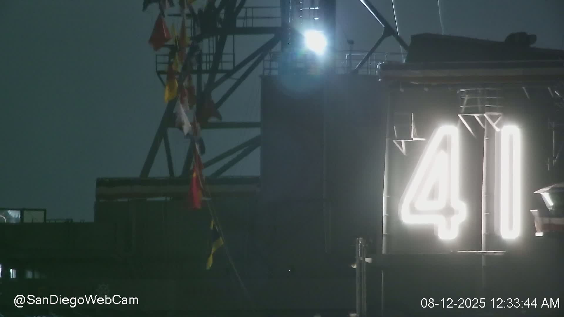 A brightly lit number 41 is visible on a dark structure at night, with several flags hanging from a crane-like apparatus in the background under a dark, possibly overcast sky.